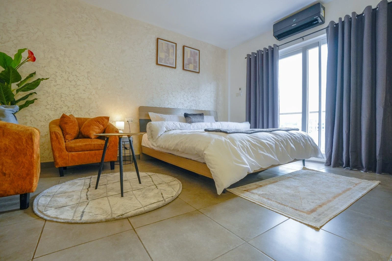 Maya Homes bedroom with a neatly prepared bed, lounge chair and balcony